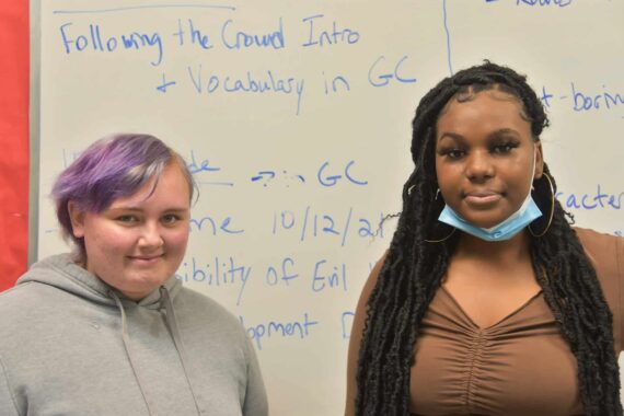 Two women posing for a picture in front of a white board.