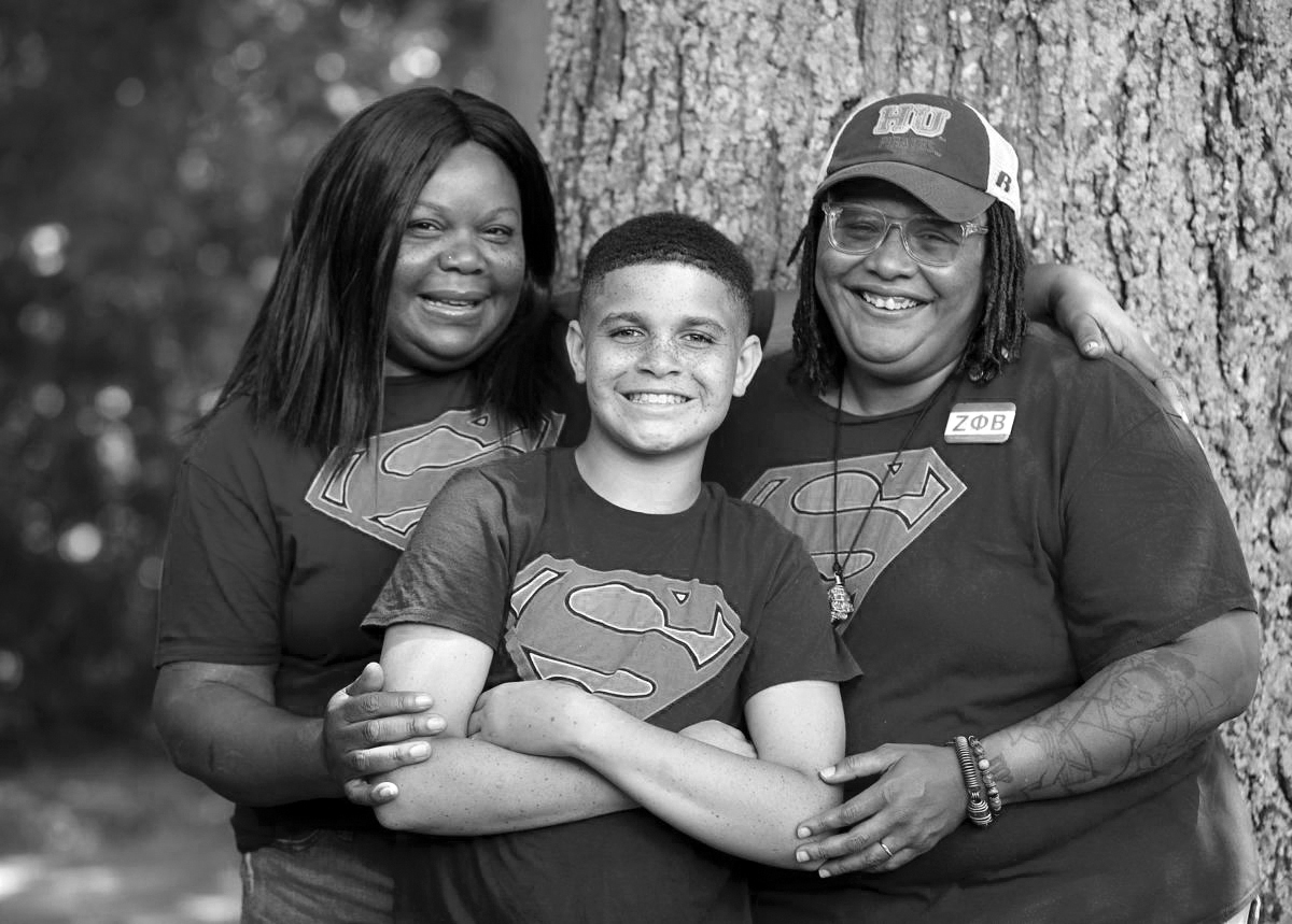 Boy standing outside by a tree with two women